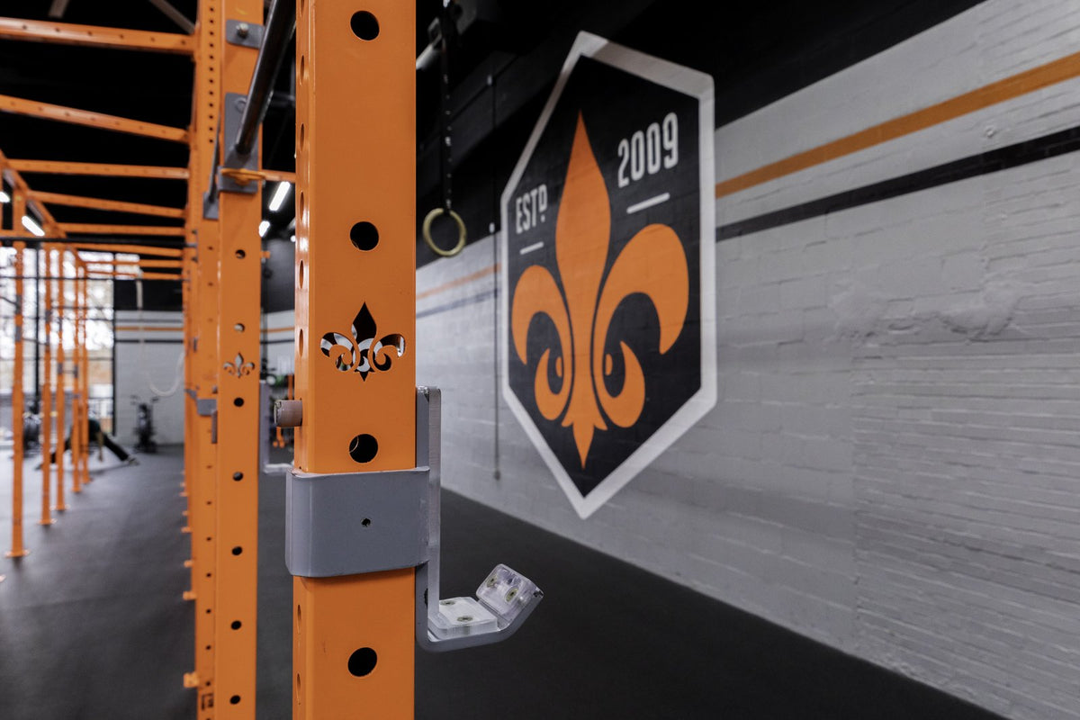 Orange BUILT rig with fleur-de-lis cutouts beside the Derby City CrossFit wall logo