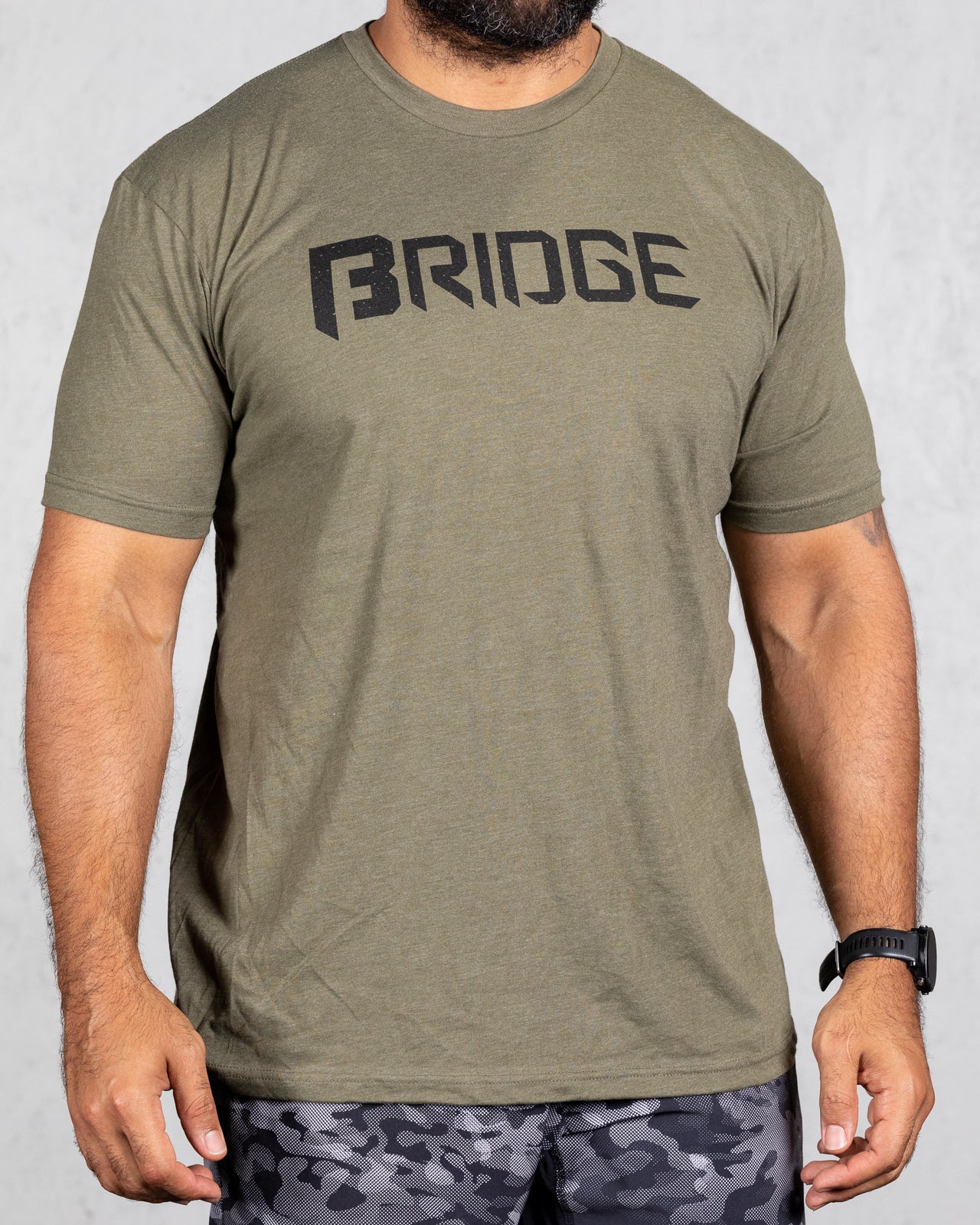 man wearing military green squad tee with bridge on the front